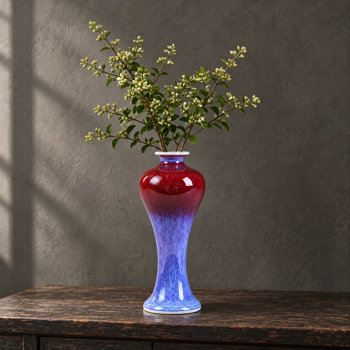 A red and purple glazed miniature porcelain vase with leafy branches on a wooden console