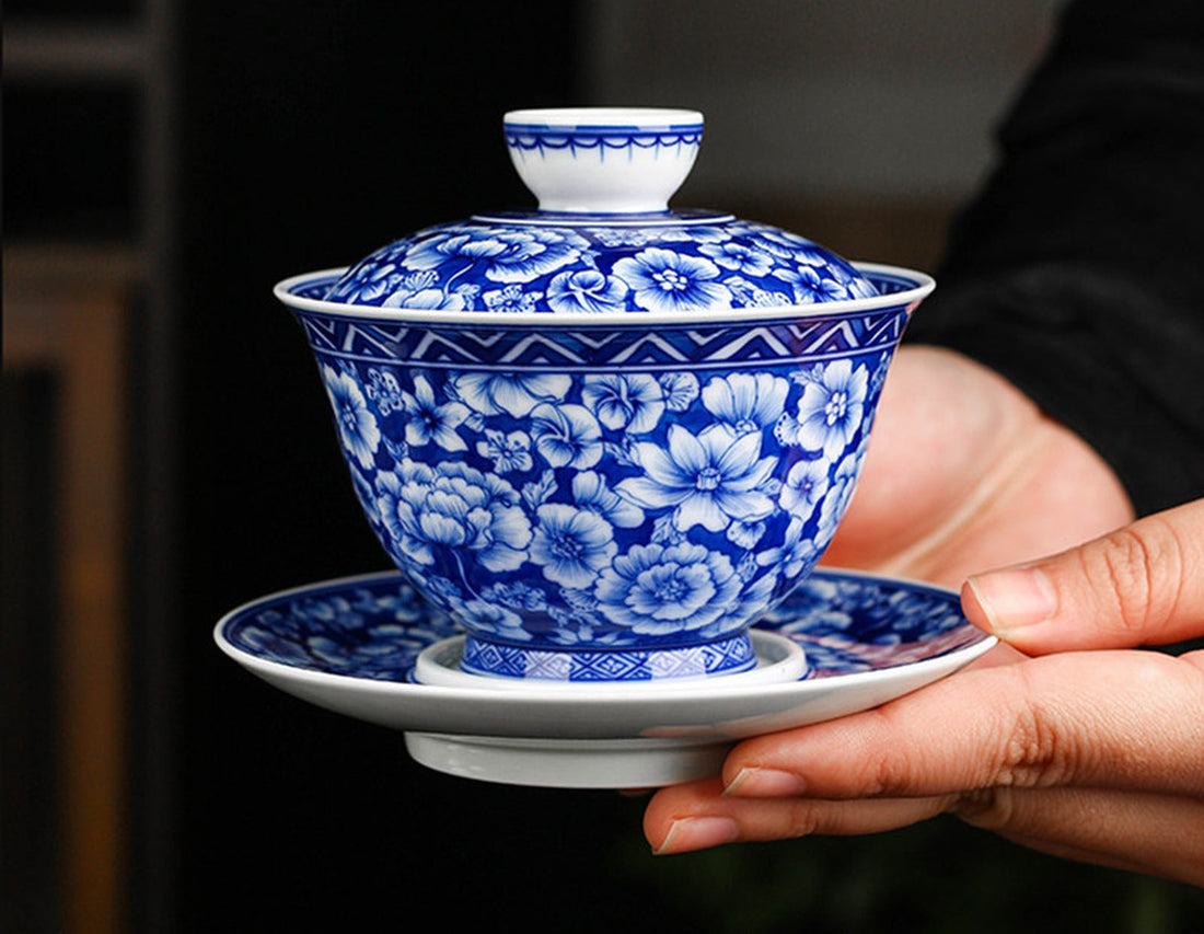 Blue-and-white floral gaiwan with a zigzag border below the rim, held on a matching saucer.