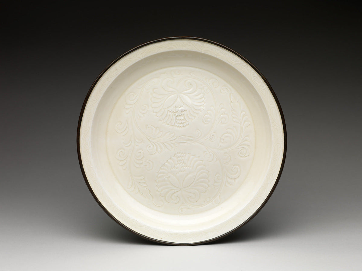 Ivory-glazed Ding ware plate with two incised chrysanthemums, curling foliage and a narrow dark copper band around the rim.
