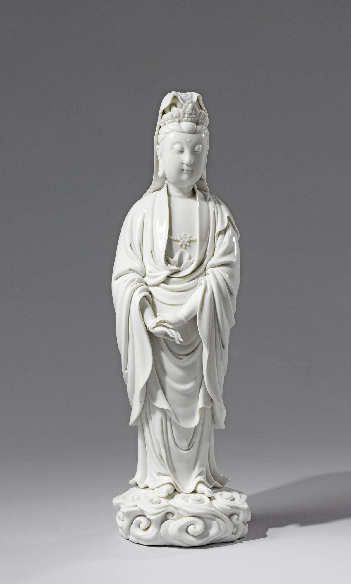 White porcelain Guanyin with lowered eyes, overlapping hands and long robes above a curled base