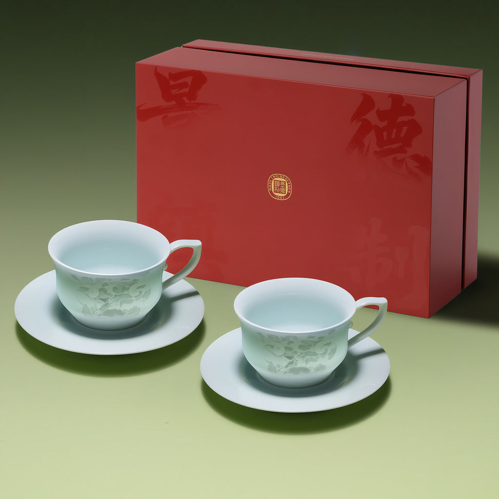 Two Qingbai horse-pattern cups and saucers beside a large red gift box.
