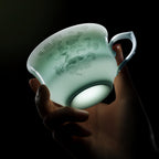 Backlit porcelain cup held in a hand, showing its translucent body and horse-and-cloud decoration.