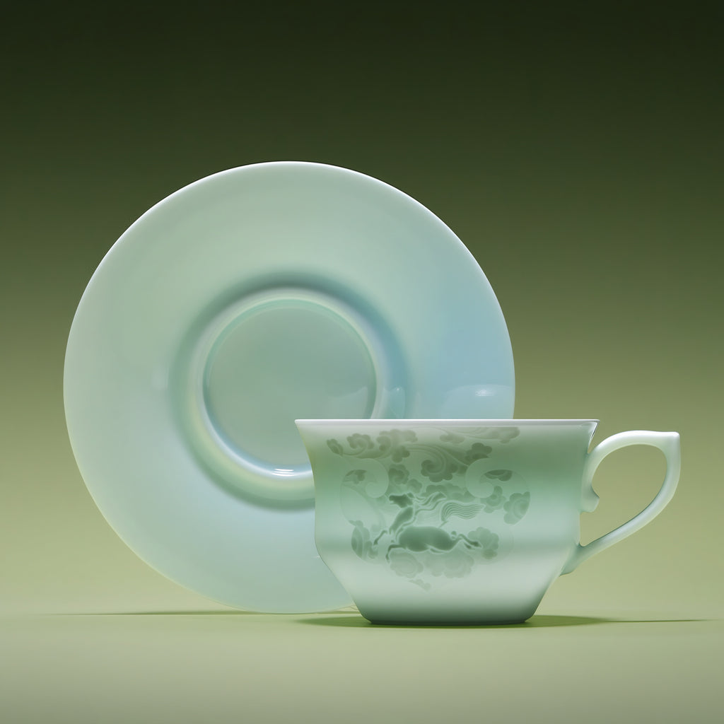 Front view of a pale Qingbai horse-pattern cup with its matching saucer standing behind it.