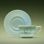 Front view of a pale Qingbai horse-pattern cup with its matching saucer standing behind it.