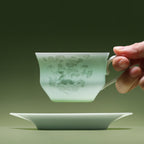 A hand holding a Qingbai horse-pattern cup by its handle above the matching saucer.