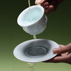 Clear water being poured through a porcelain cup onto its matching saucer.