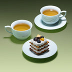 Two Qingbai horse-pattern cups filled with tea, with a dessert on one matching saucer.