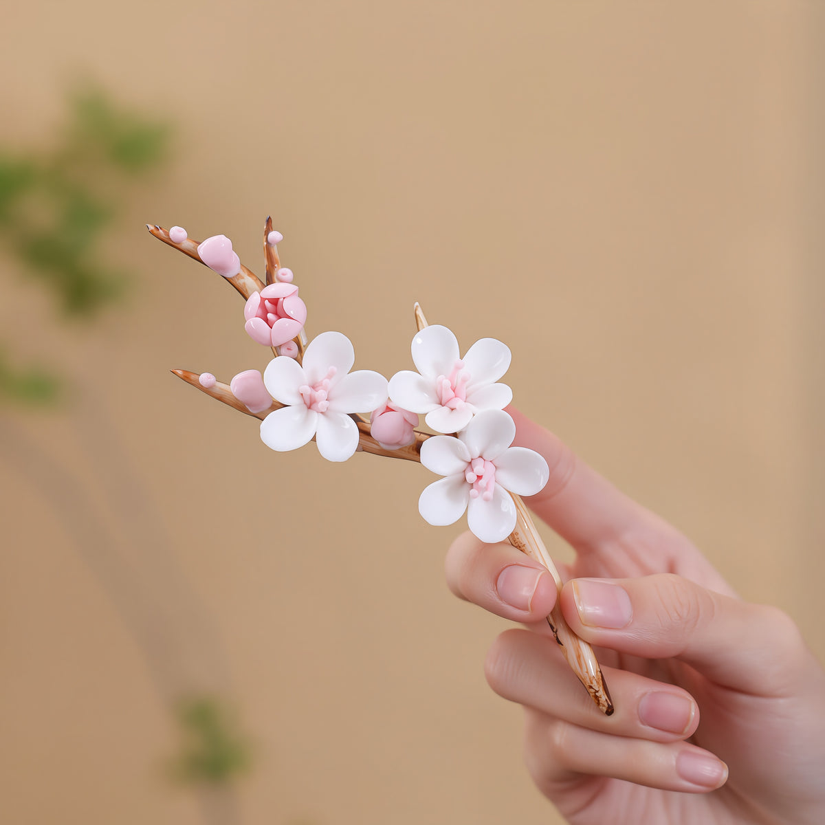 Hand holding a ceramic plum branch with white flowers, pink centers and buds, and brown stems.