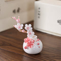 White porcelain plum-blossom vase with a white-and-pink ceramic branch on a wooden table.