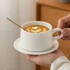 Two-hand view of the 240 ml white porcelain coffee cup, saucer, and spoon