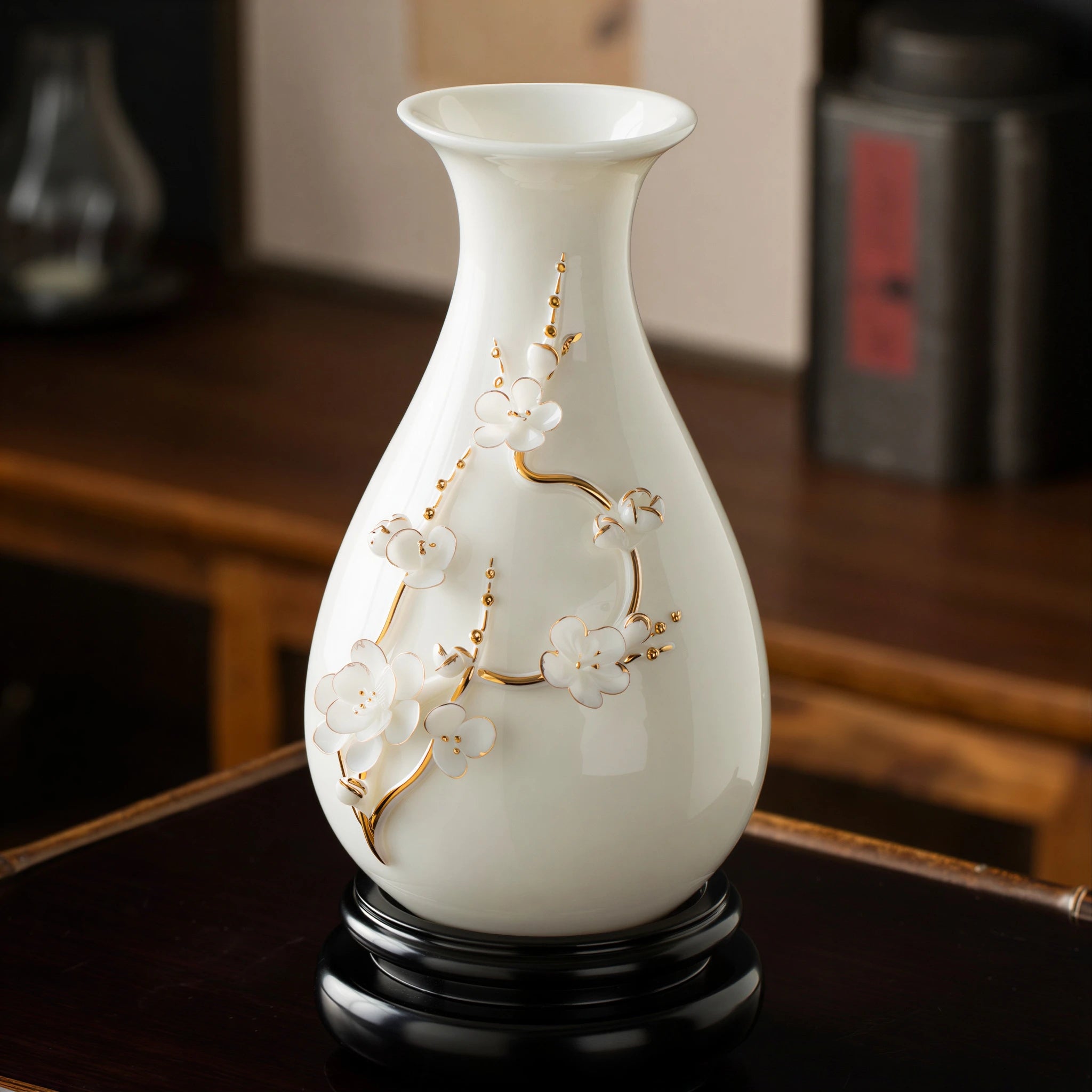 White and gold-toned plum blossom relief vase displayed on a dark wood base