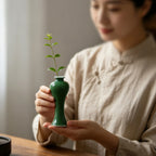 Hand holding a small emerald-green Meiping porcelain vase with a single cutting.
