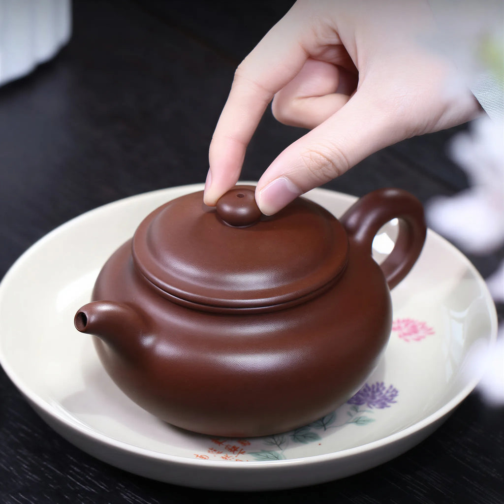 Hand lifting the fitted lid from the Fanggu teapot