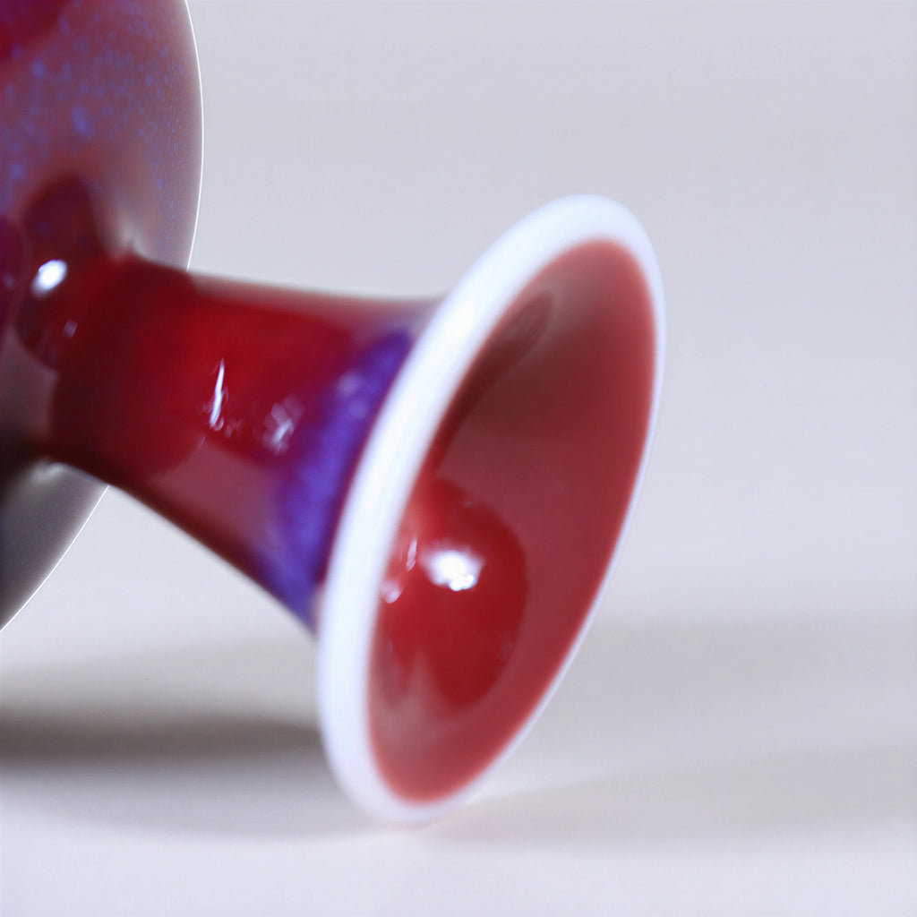 Close view of a flared white foot and glossy rose-purple glaze.