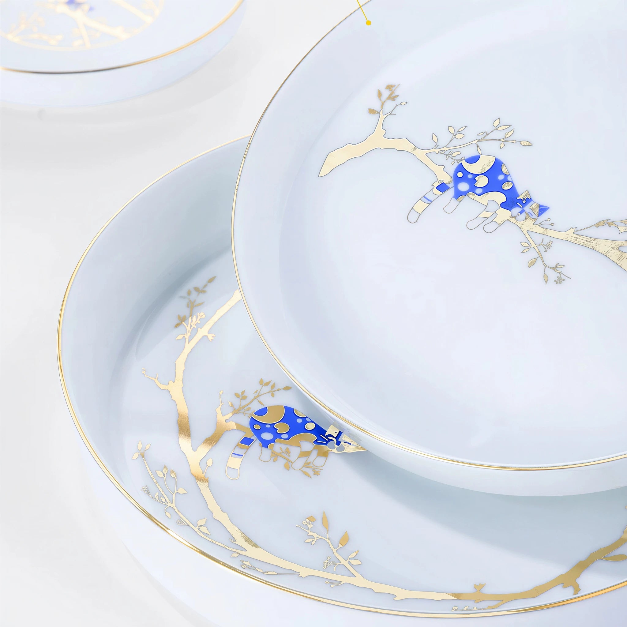 Close detail of the cobalt-blue resting cat and gold branch motif across two white porcelain plates.