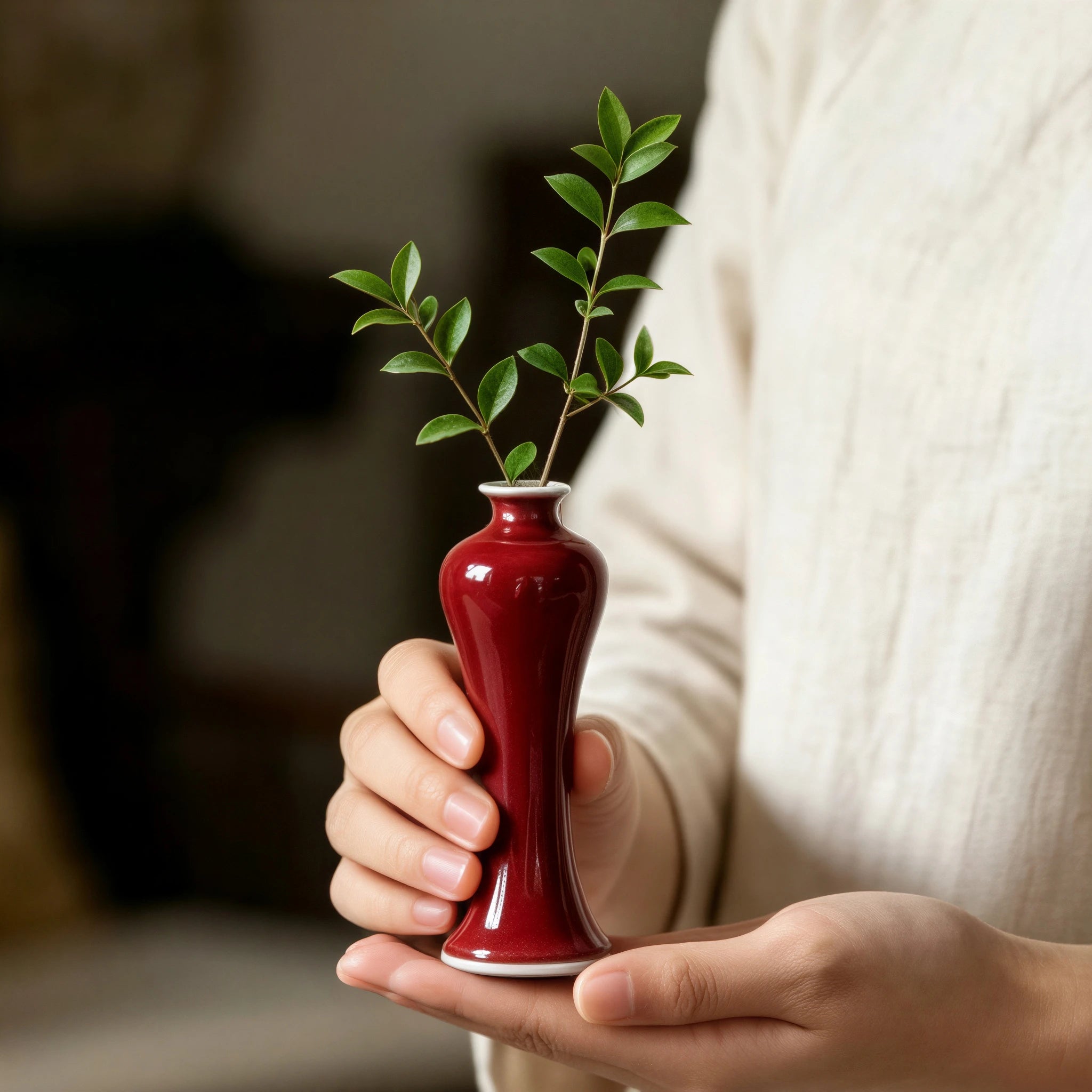Handheld oxblood red porcelain vase with a small green cutting