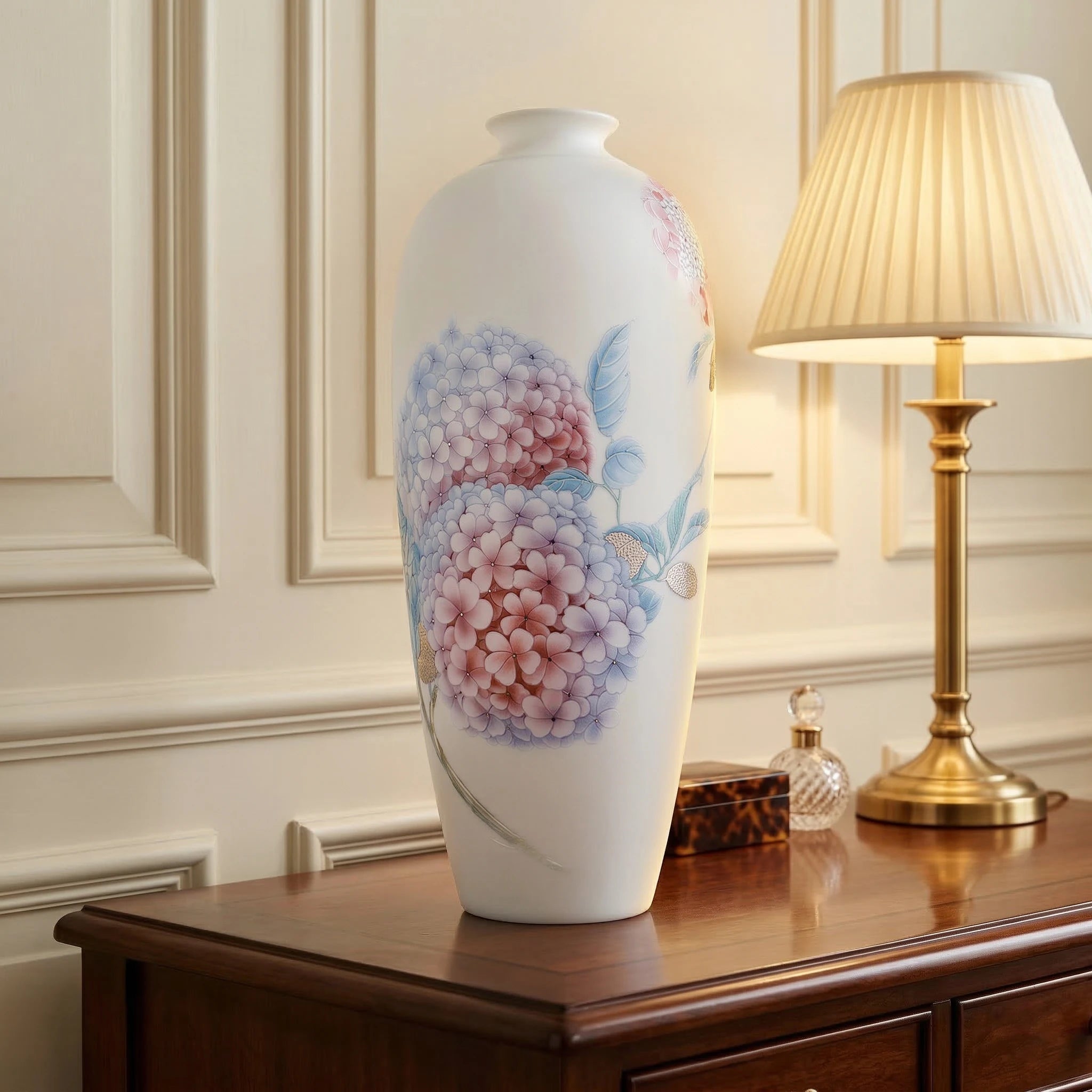 White porcelain hydrangea Meiping vase displayed beside a brass table lamp on a wood sideboard