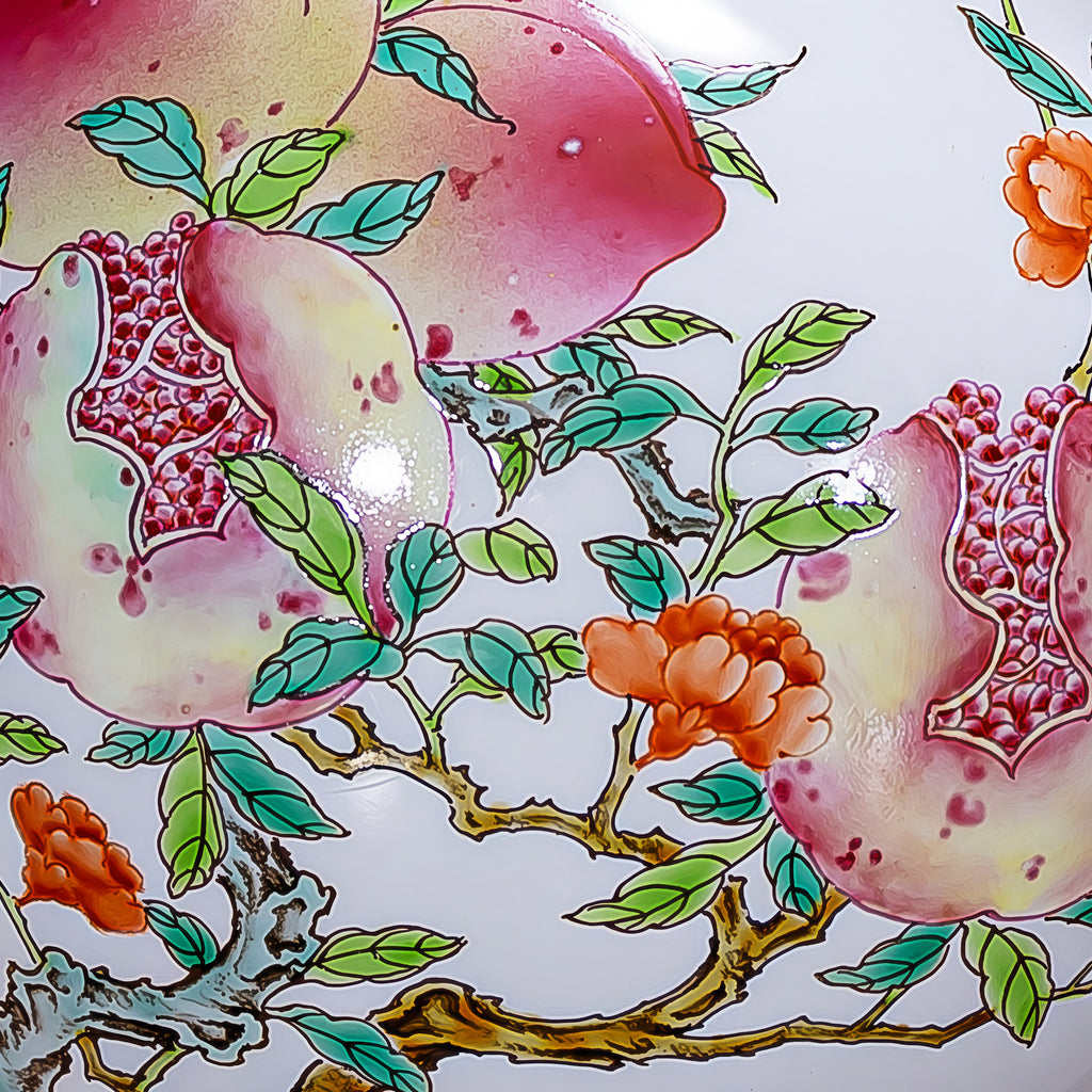 Close view of pink fruit, red pomegranate seeds, orange flowers and green leaves on the porcelain vase.