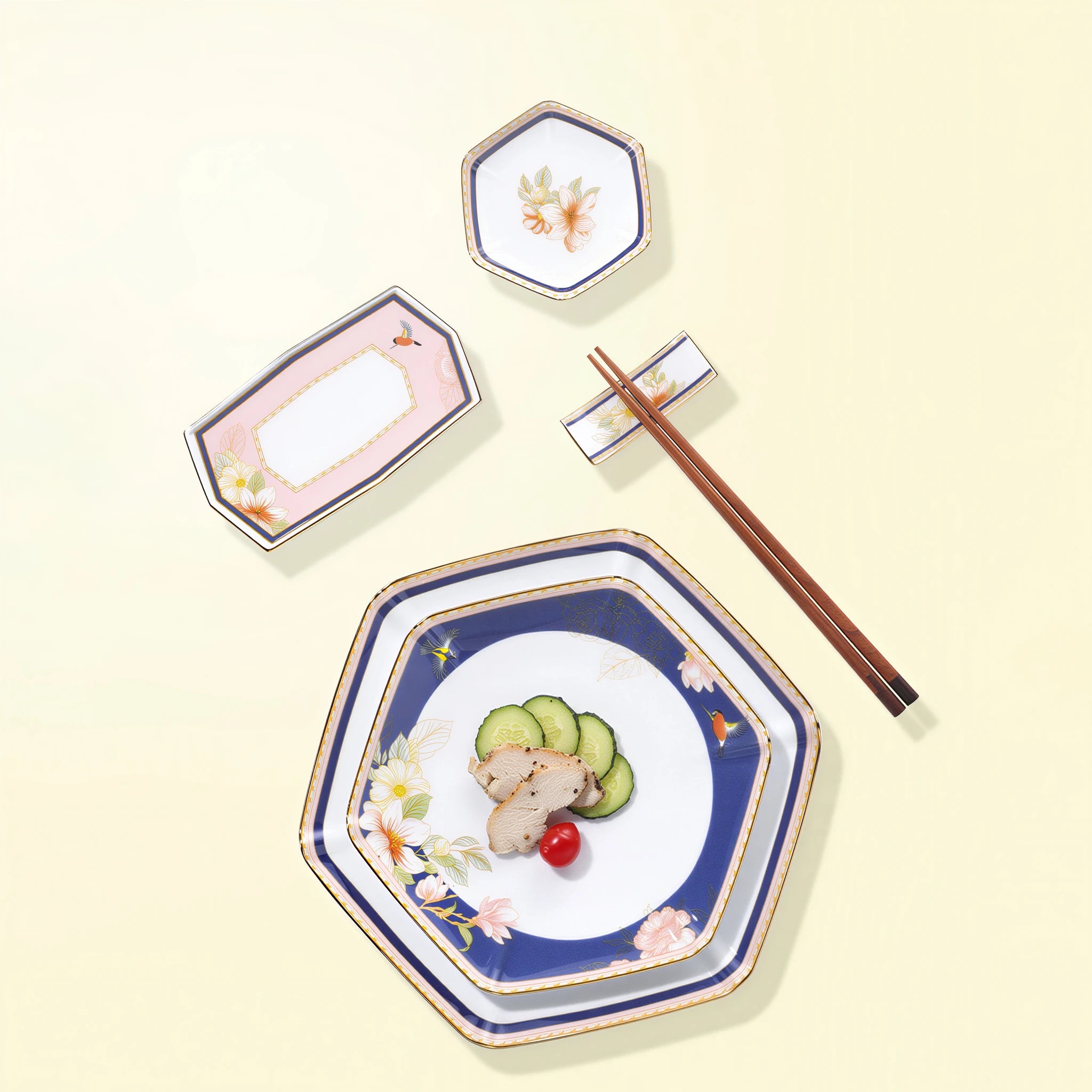 Overhead arrangement of faceted floral porcelain plates, condiment dish, napkin tray, chopstick rest, and styling chopsticks.