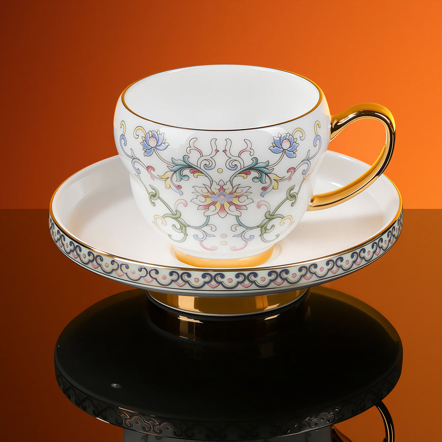 Floral porcelain cup on a matching footed saucer, with a gold-tone handle and rim against an orange background.