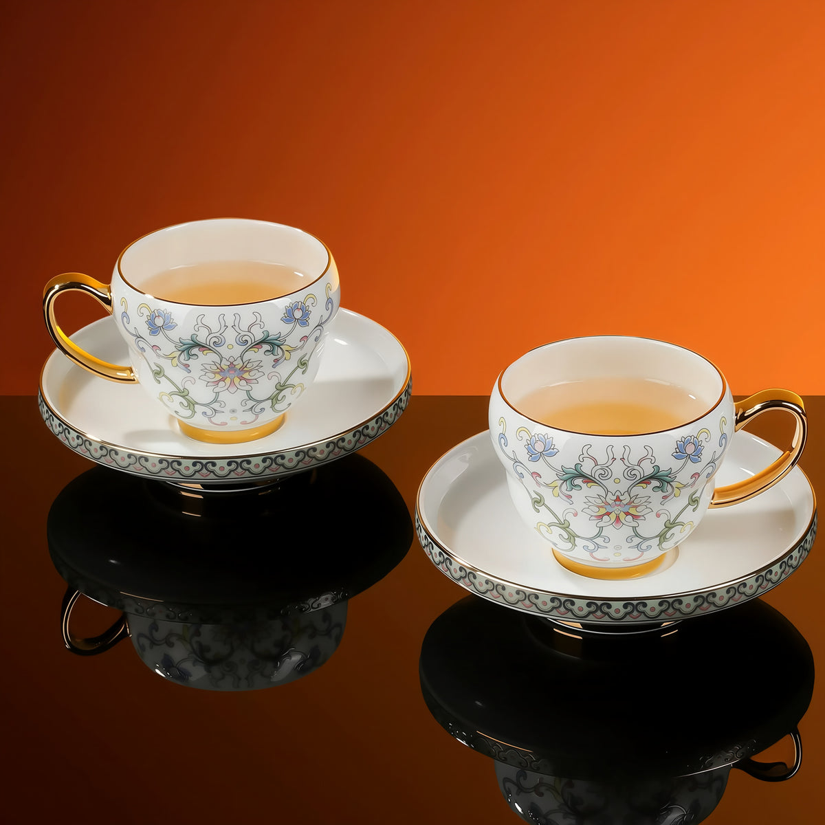 Two floral porcelain cups filled with tea on matching footed saucers, with gold-tone handles and rims.