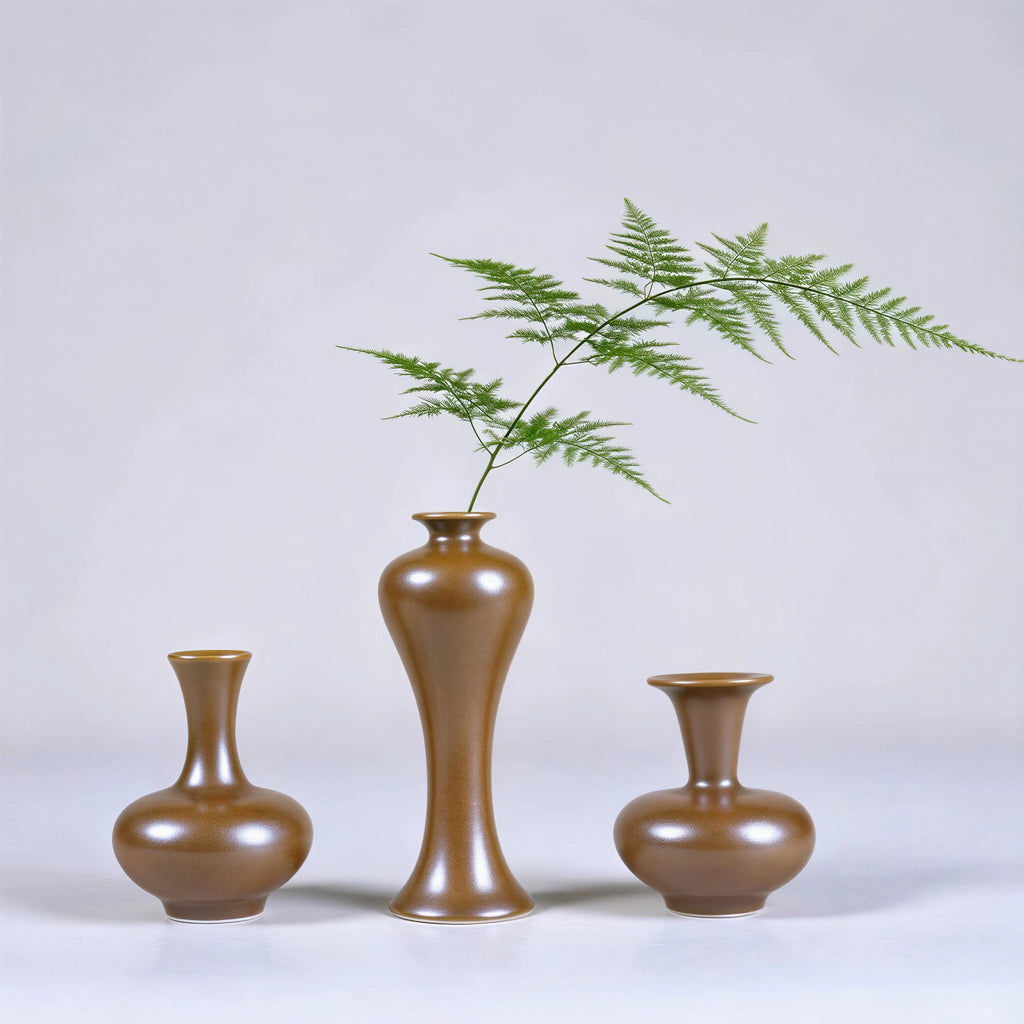 Three small Jingdezhen maple-yellow porcelain vases with a fern stem.