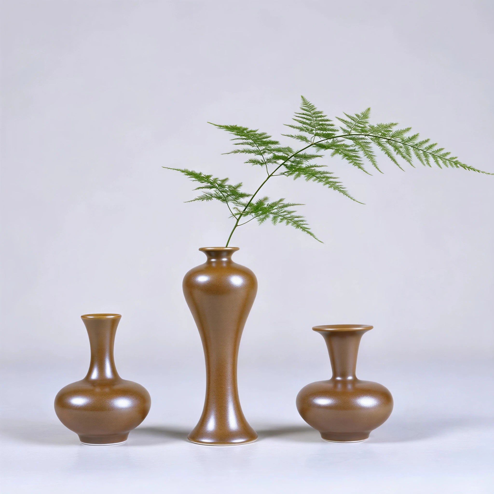 Three small Jingdezhen maple-yellow porcelain vases with a fern stem.