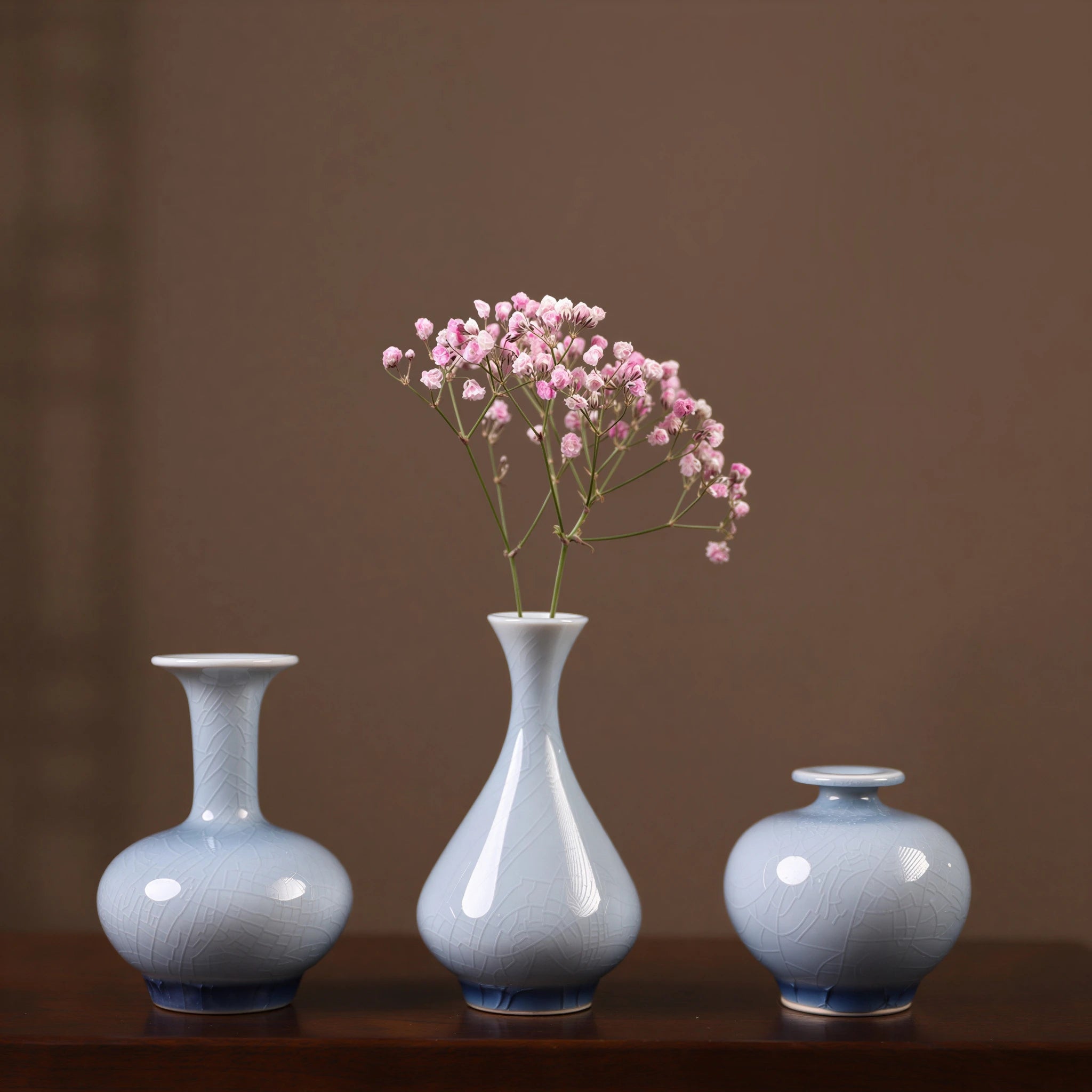 Three pale-blue crackle-glaze Jingdezhen vases with a small pink flower spray.