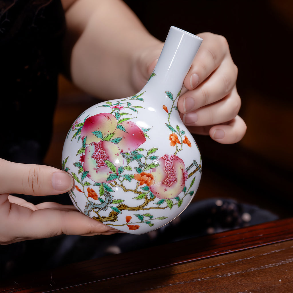 Small peach and pomegranate Tianqiu vase held in two hands, showing its tabletop scale.