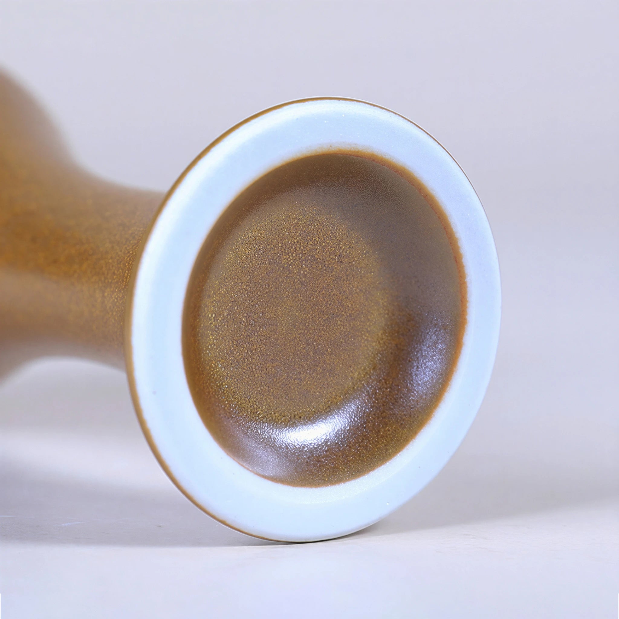 Close view of the white base on a glossy maple-yellow porcelain vase.