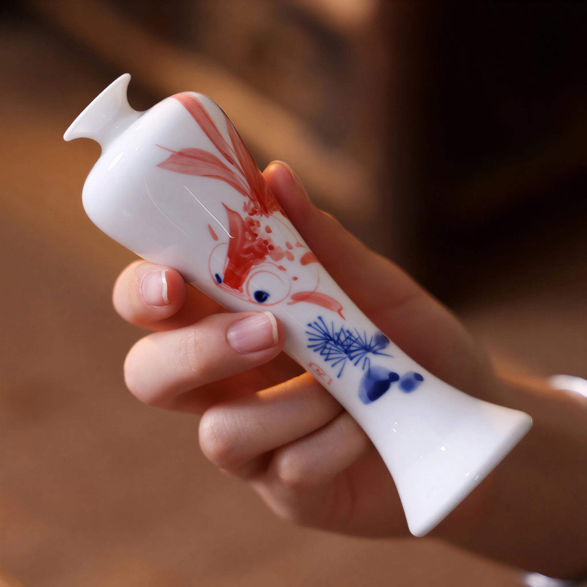 Close-up of a slim hand-painted goldfish Meiren vase held in one hand