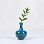 Globular peacock green porcelain vase with a single leafy stem