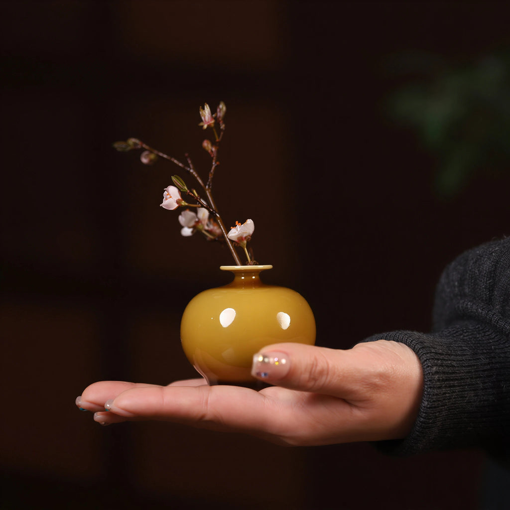 Round luminous yellow porcelain vase with blossom branch held in one hand