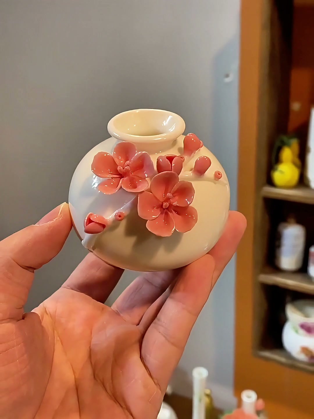 Handheld view of a miniature white porcelain vase with raised pink plum blossoms and buds.