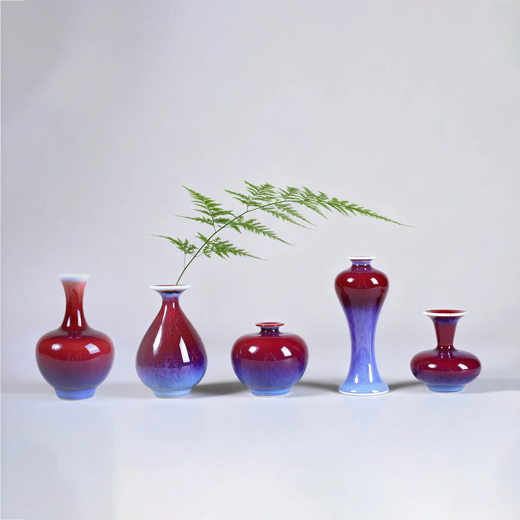 Five small rose-purple Jingdezhen porcelain vases arranged with fine green stems.