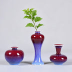 Three rose-purple mini porcelain vases arranged with green cuttings.