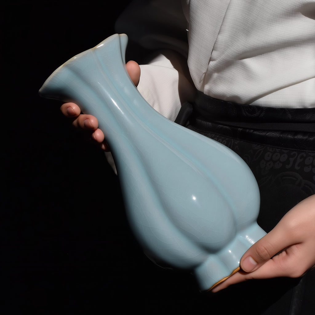 Haitang vase tilted in two hands, showing the curved lobes, sky-blue crackle glaze and scalloped foot.