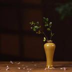 Slender luminous yellow porcelain meiping vase with small branch on a wood table