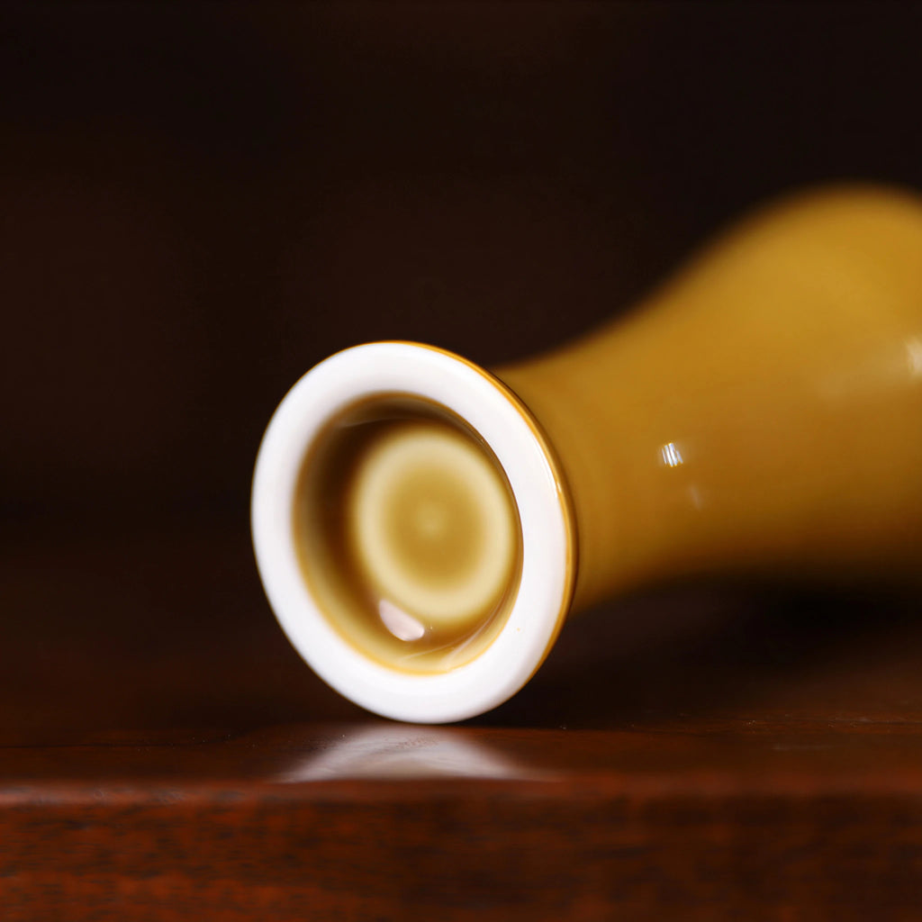 Foot ring detail of a small luminous yellow porcelain vase on dark wood