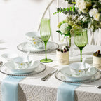 Spring Dawn porcelain plates and bowls arranged for two on a white table with green stemware and floral styling.