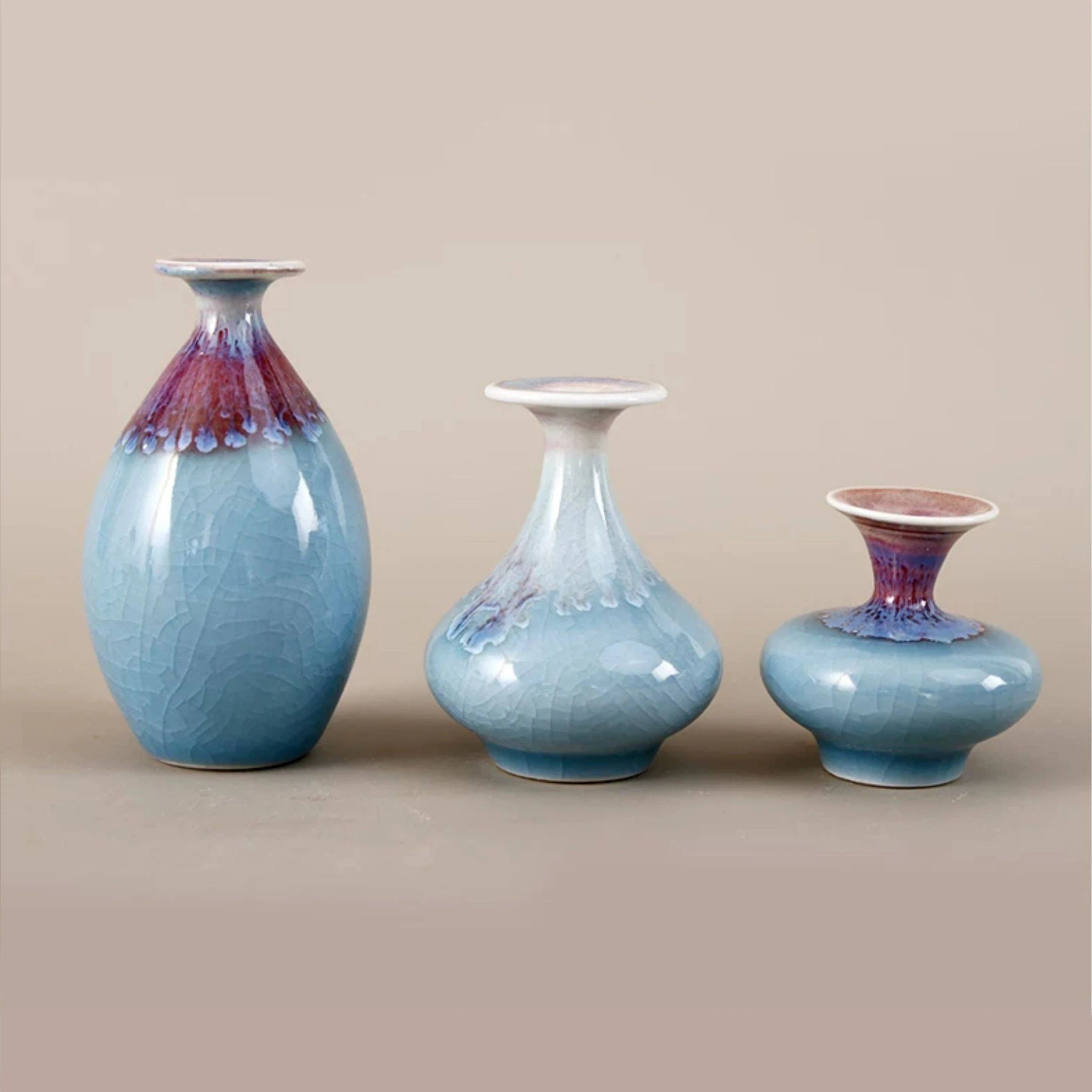 Three blue reactive glaze miniature porcelain vases arranged on a neutral tabletop