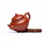 Angled view of the rounded red zisha body, handle and spout